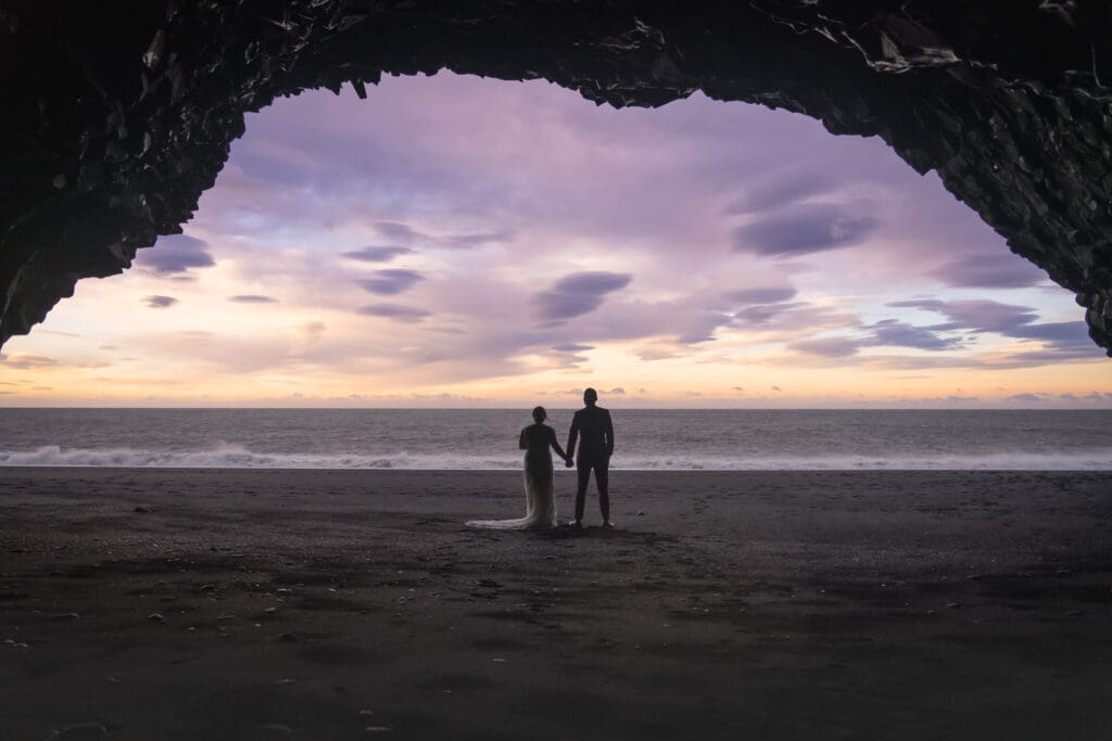 Elopement couple seen through a cave at black sand beach in Iceland