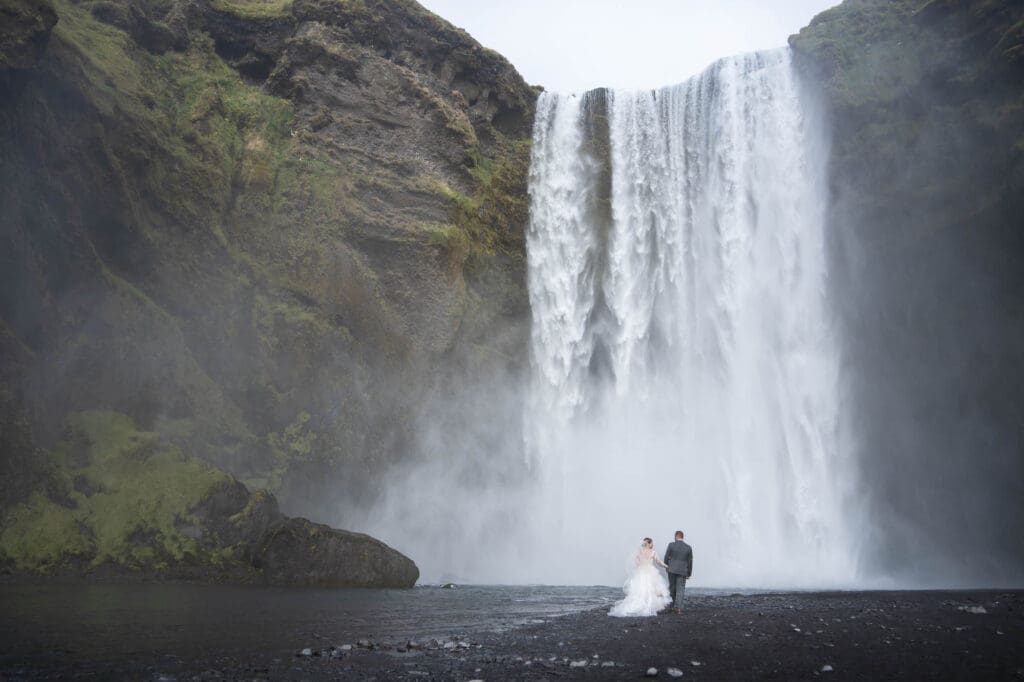 Couple in wedding attire walking towards Skogafoss in Iceland