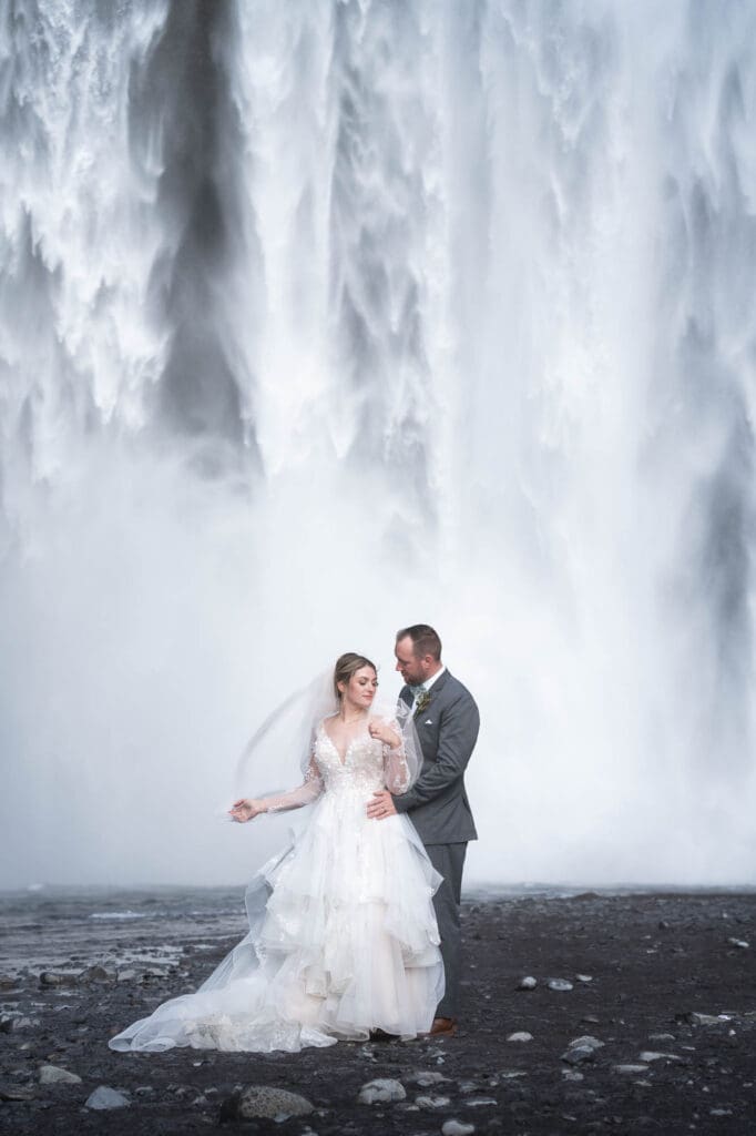 A couple in wedding attire in front of Skogafoss waterfall in Iceland