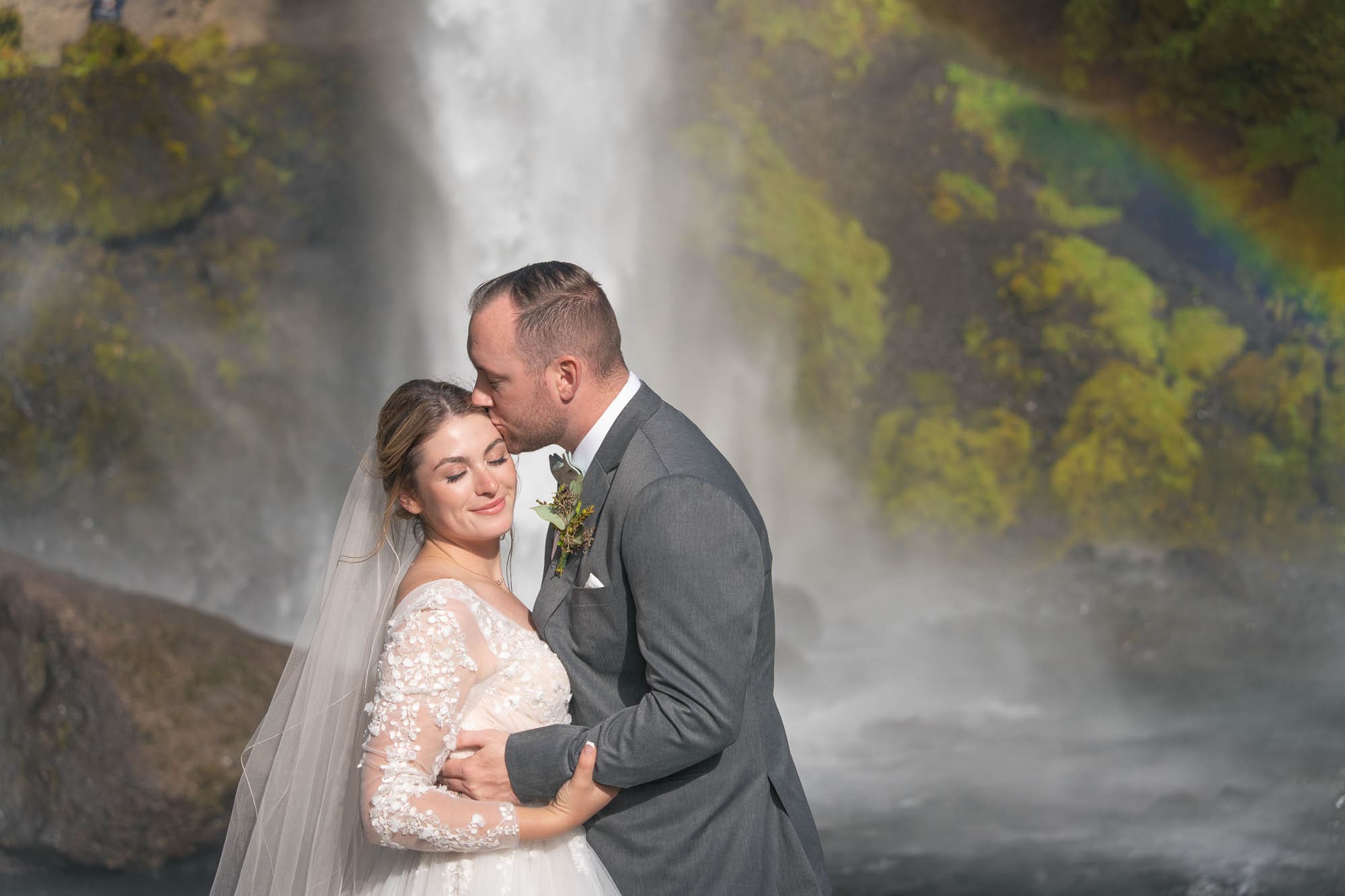 Closeup of a bride and groom in front of waterfall in Iceland with a rainbow behind them