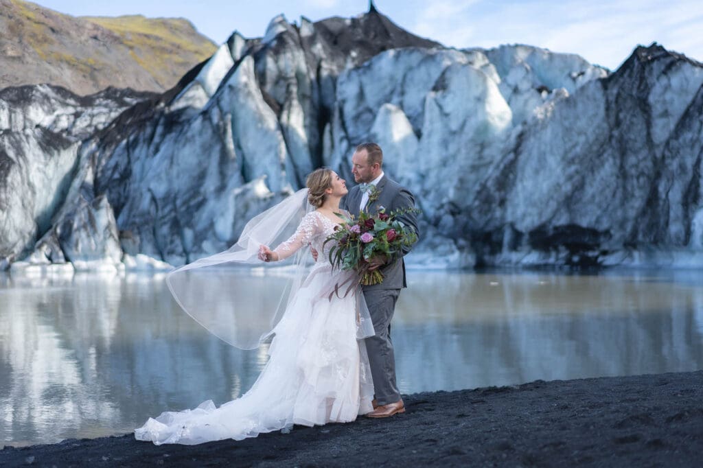 A couple in wedding attire is standing by the glacier lagoon in front of Solheimajokull in Iceland