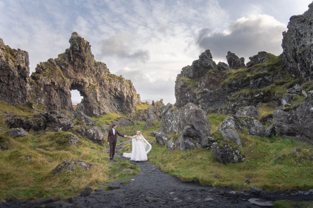 Couple in wedding attire is walking holding hands in Snaefellsnes Peninsula in Iceland