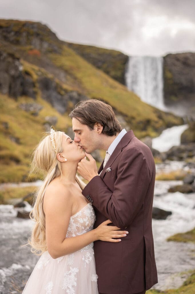Couple in wedding attire kissing in front of a waterfall in Snaefellsnes Peninsula in Iceland